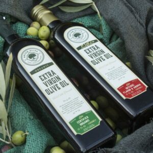Premium Grade A Extra Virgin Olive Oil in dark glass bottle – rich golden-green color, unfiltered sediment, olive branch, pour spout, fresh salad background